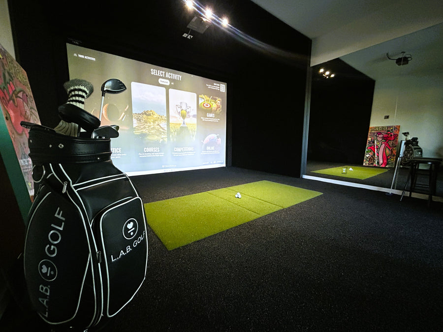 Golf simulator setup with screen displaying game options and golf bag in foreground.