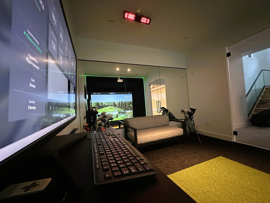 Indoor golf simulator setup with large screen, keyboard, and sofa in a room.