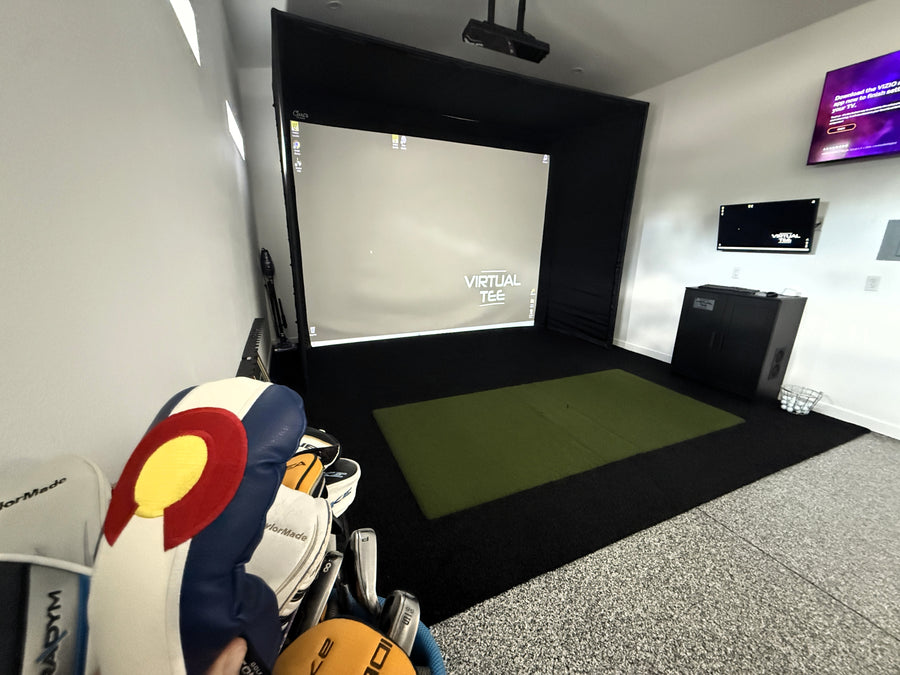 Golf simulator setup with golf clubs and a screen displaying 'Virtual Tee'.