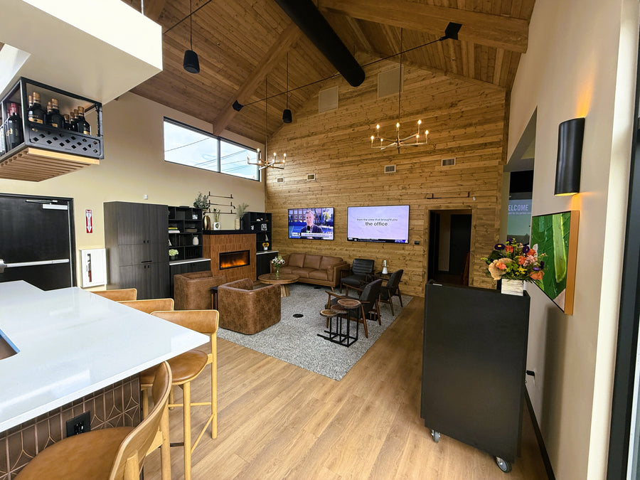 Modern living room with wooden floors, a kitchen area, and multiple televisions.