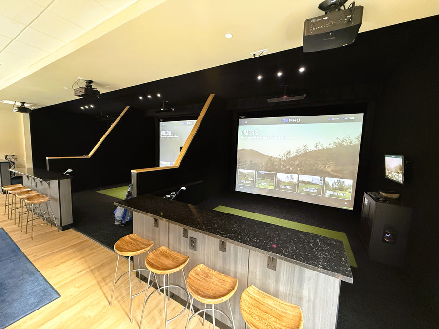 Modern golf simulator setup with multiple screens and bar stools.