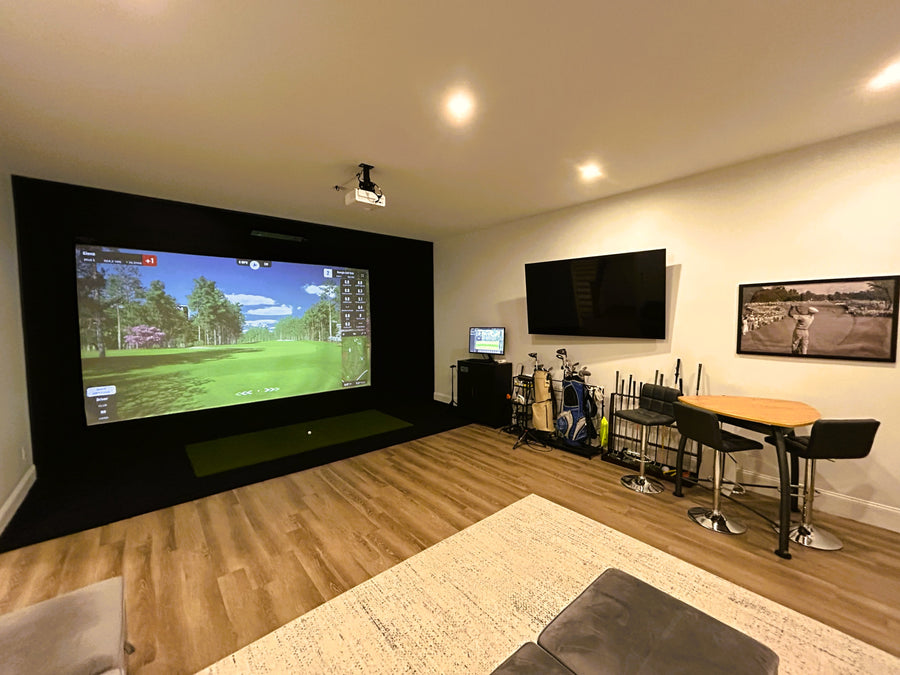 Golf Simulator room with large screen displaying a golf simulation game, surrounded by gaming equipment and furniture.