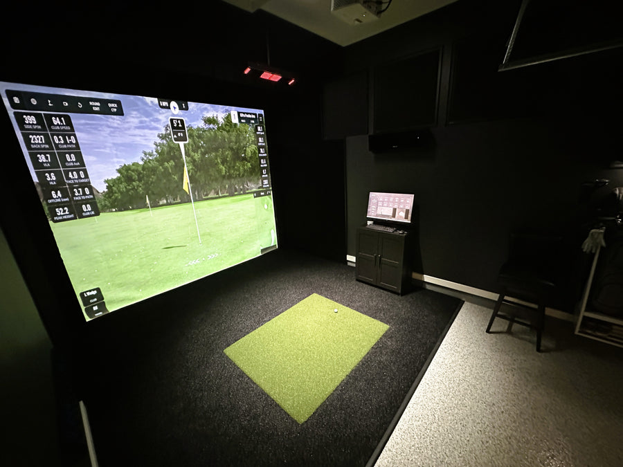 Golf simulator setup in a dark room with a large screen displaying a golf course.