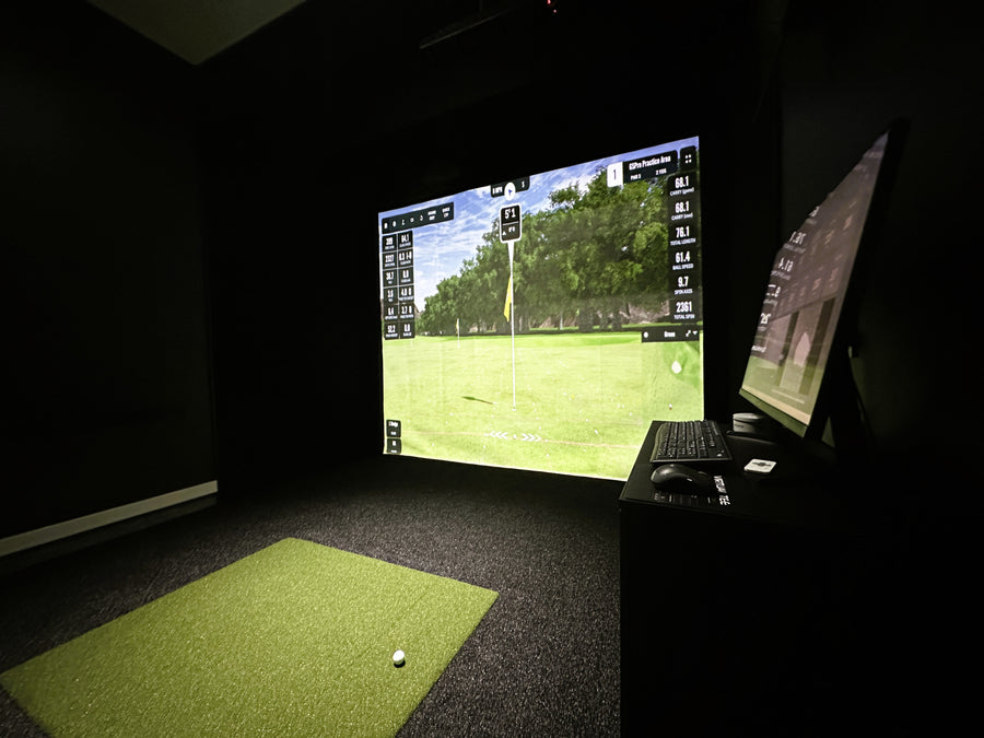 Golf simulator setup with screen displaying a golf course and grass mat on the floor.