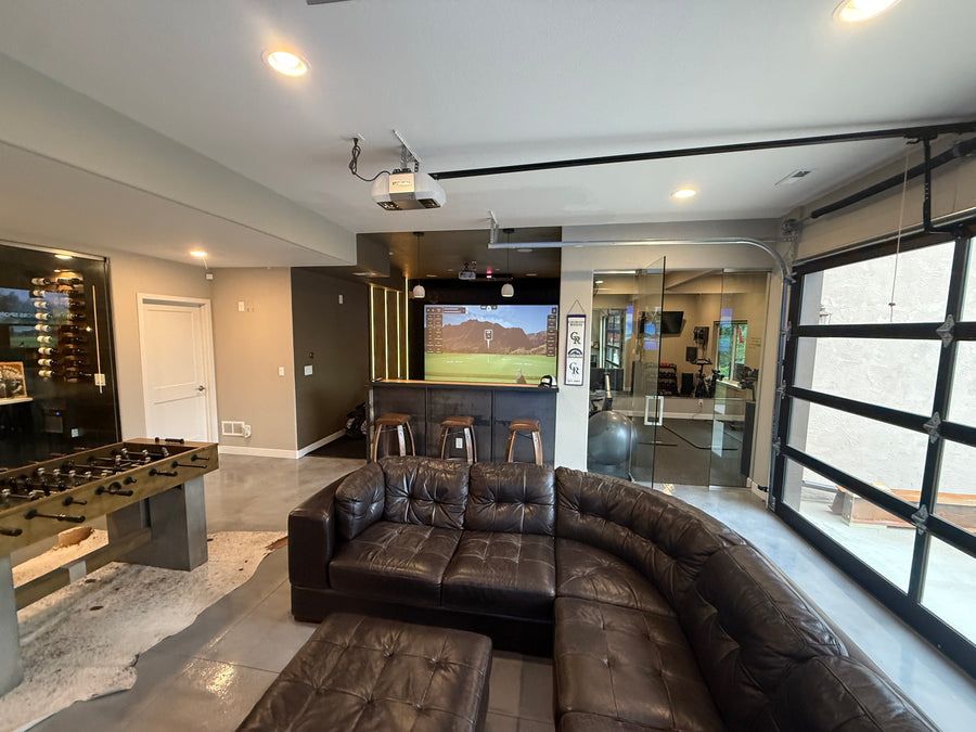 Modern living room with leather sofa, foosball table, and a golf simulator.