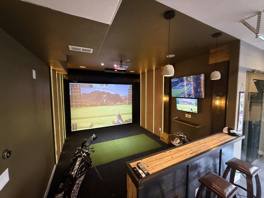 Golf simulator setup in a room with multiple screens and golf equipment.