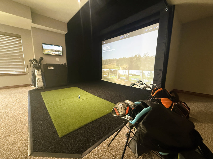 Indoor golf simulator setup with green mat and golf clubs in a room.