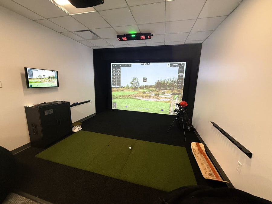 Golf simulator room with screen displaying a golf course and TV on wall.