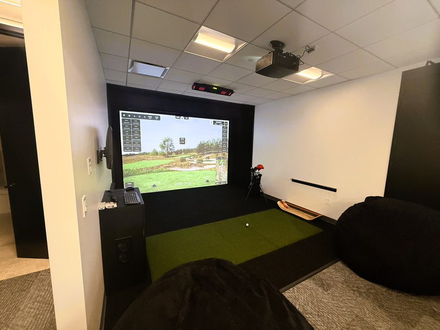 Golf simulator setup in an office space with a screen displaying a golf course.
