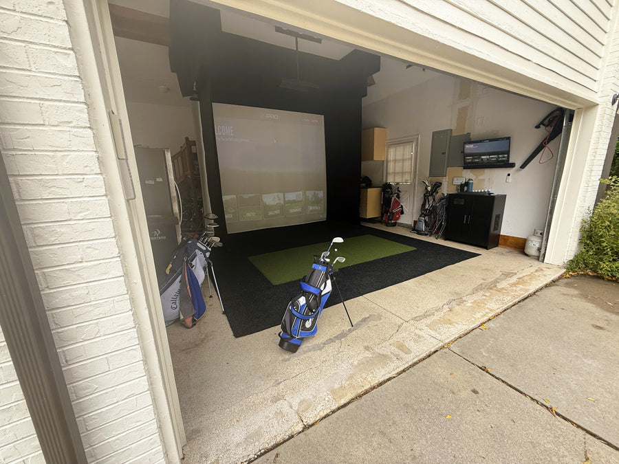 Indoor golf simulator setup in a garage with a screen and golf equipment.