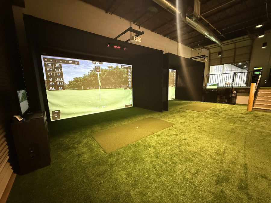 Indoor golf simulator with large screen displaying a golf course.