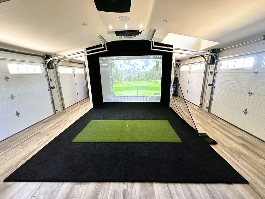 Indoor golf simulator setup in a garage with a green mat and screen displaying a golf course.