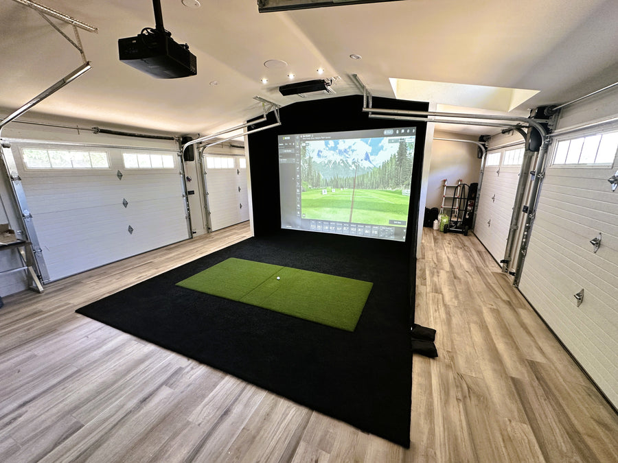 Indoor golf simulator setup in a garage with a screen displaying a golf course.