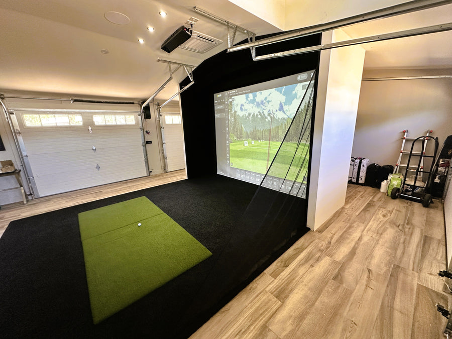 Indoor golf simulator setup in a garage with a screen displaying a golf course.