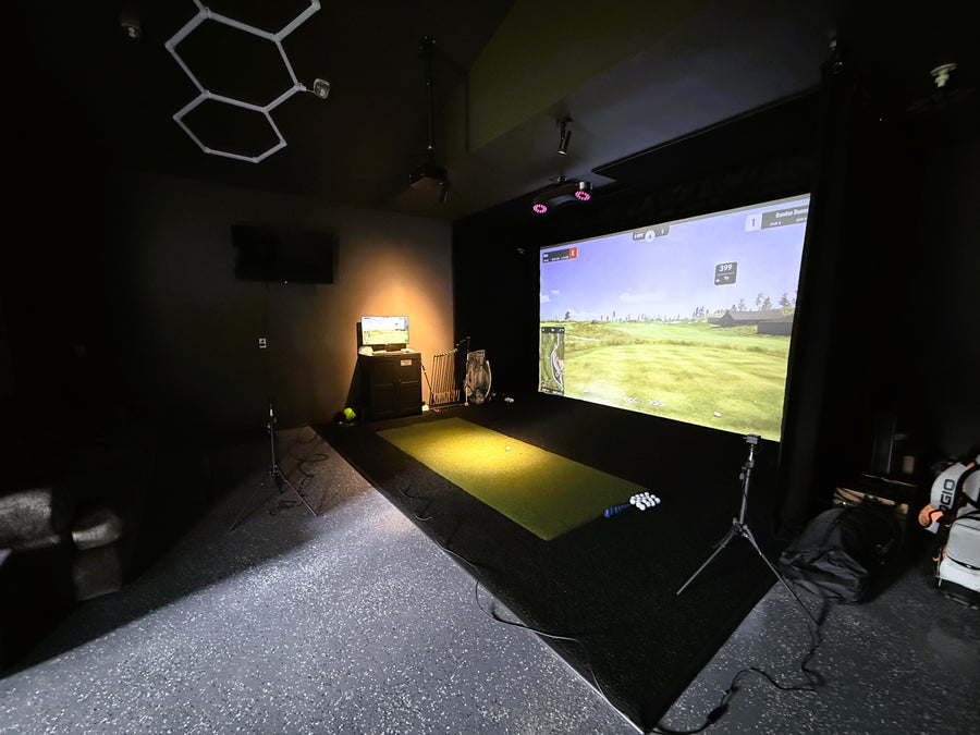 Indoor golf simulator setup with screen displaying a golf course.