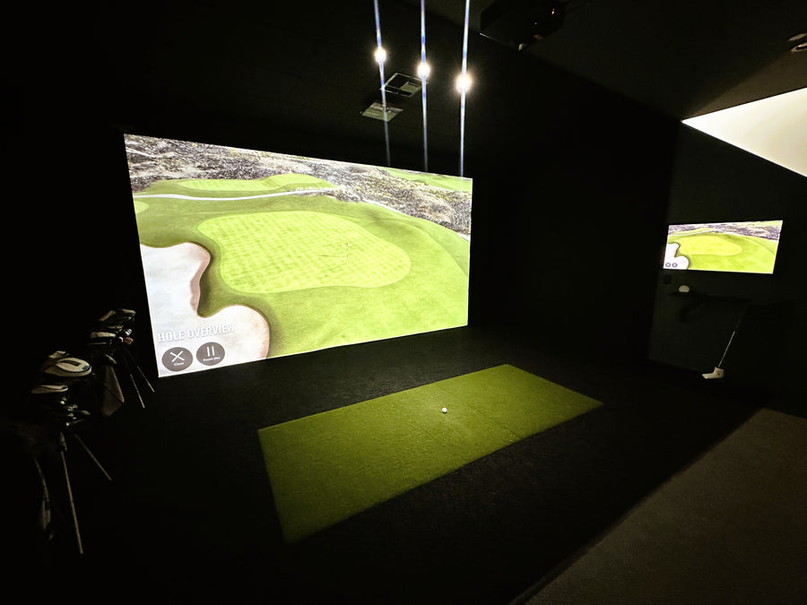 Golf simulator setup with screen displaying a golf course and practice mat.