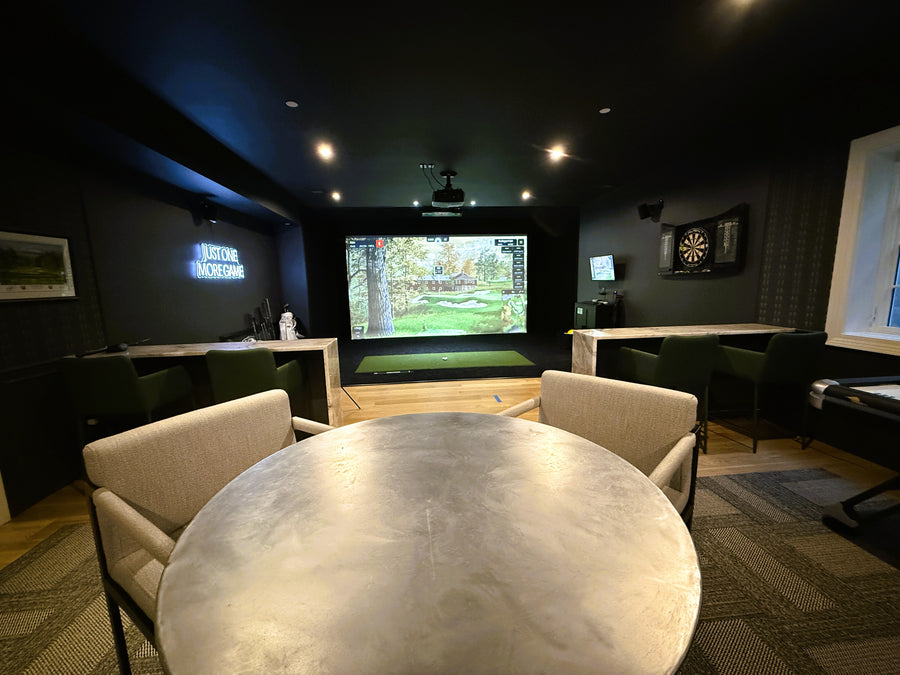 Golf simulator with a round table and comfortable chairs.