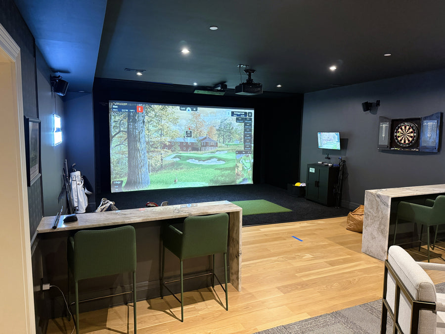 Golf simulator room, surrounded by chairs and a bar area.
