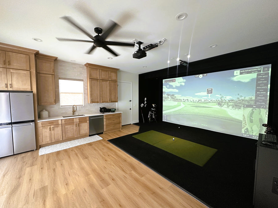 Golf simulator setup in a modern kitchen with a large screen displaying a golf course.