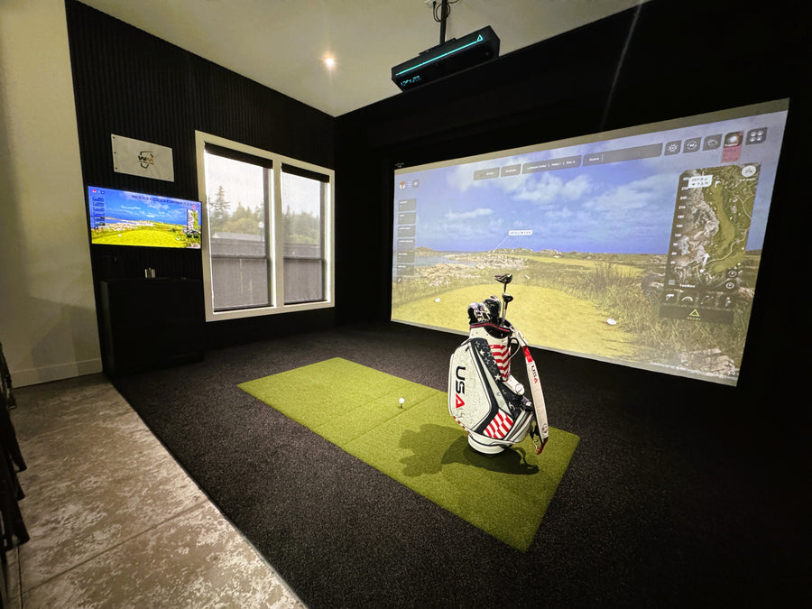 Golf simulator setup with projection screen and golf bag on a green mat.