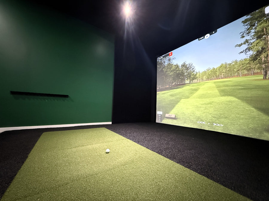 Indoor golf simulator setup with screen displaying a golf course and ball on the floor.