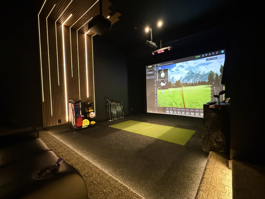 Indoor golf simulator setup in a dark room with a screen displaying a golf course.