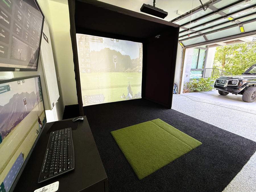 Simulator setup with multiple screens and a green mat in a garage.