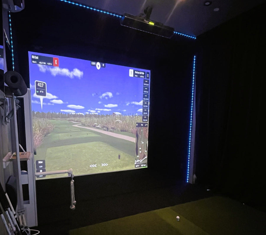 Golf simulator setup with screen displaying a golf course on a dark background
