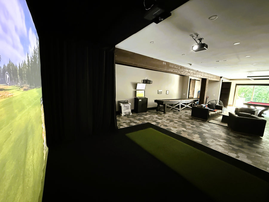 Indoor golf simulator setup in a modern living room with a large screen displaying a golf course.