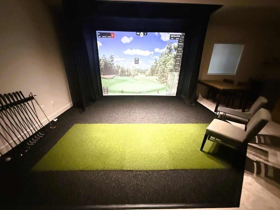 Golf simulator setup with screen displaying a golf course and green mat on the floor.