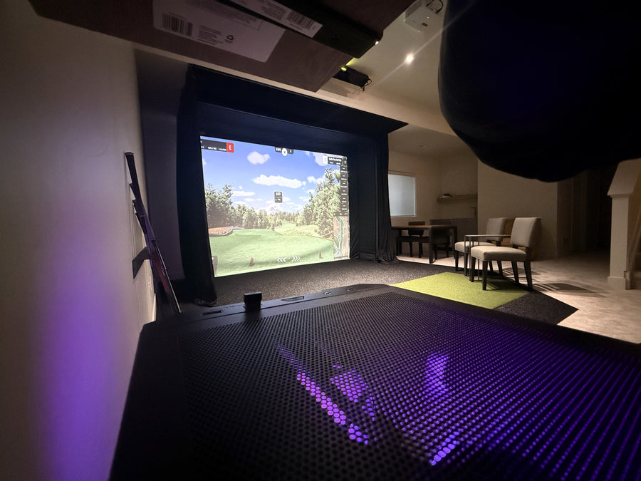 Indoor golf simulator setup with screen displaying a golf course.
