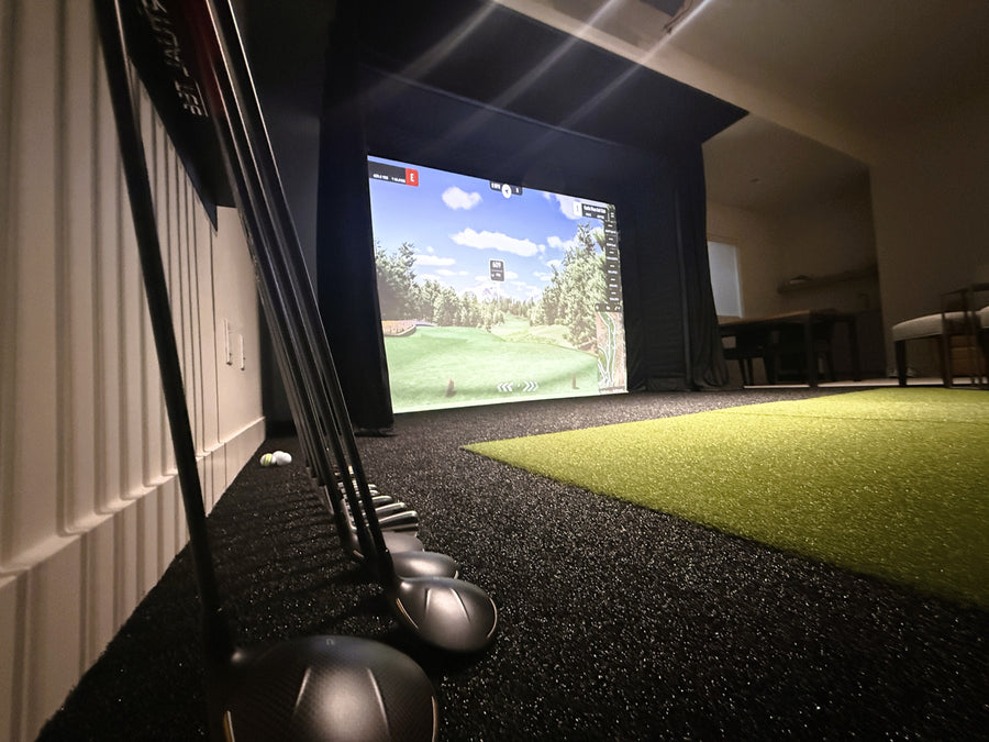Golf simulator setup with golf clubs and screen displaying a golf course.