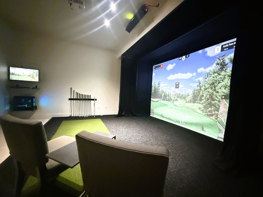 Indoor golf simulator setup with large screen and chairs in a room.