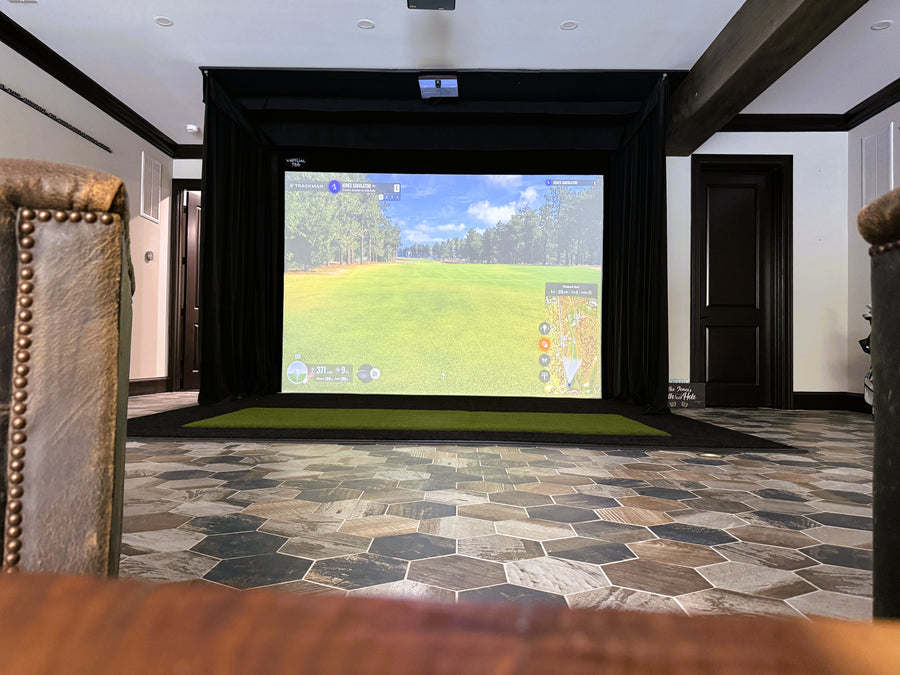 indoor golf simulator setup with black turf, a custom screen, and curtains.