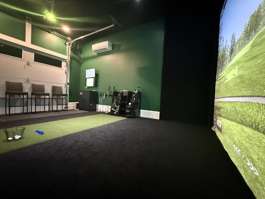Indoor golf simulator setup with green walls and a screen displaying a golf course.