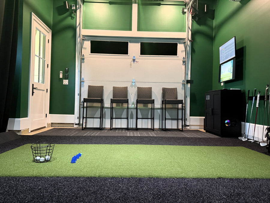 Golf simulator setup with green turf, balls, and TV on a green wall.