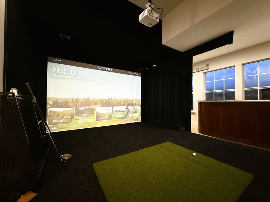 Indoor golf simulator room with screen displaying a golf course and green floor.