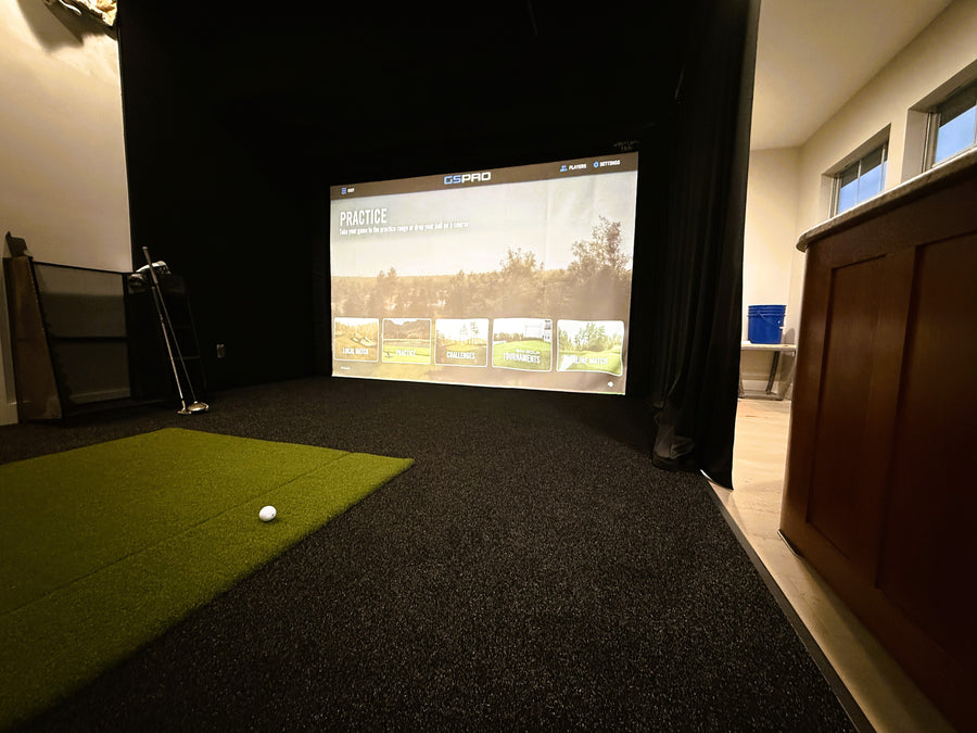 Golf simulator setup with screen displaying a golf course and green mat on the floor.