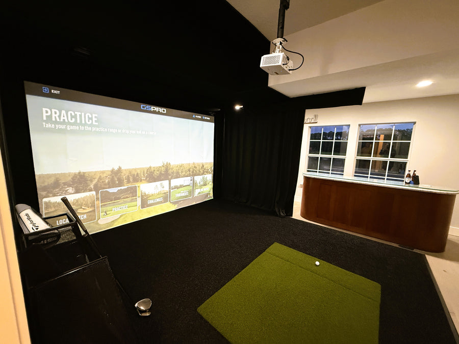 Indoor golf simulator setup with screen, projector, and green mat.