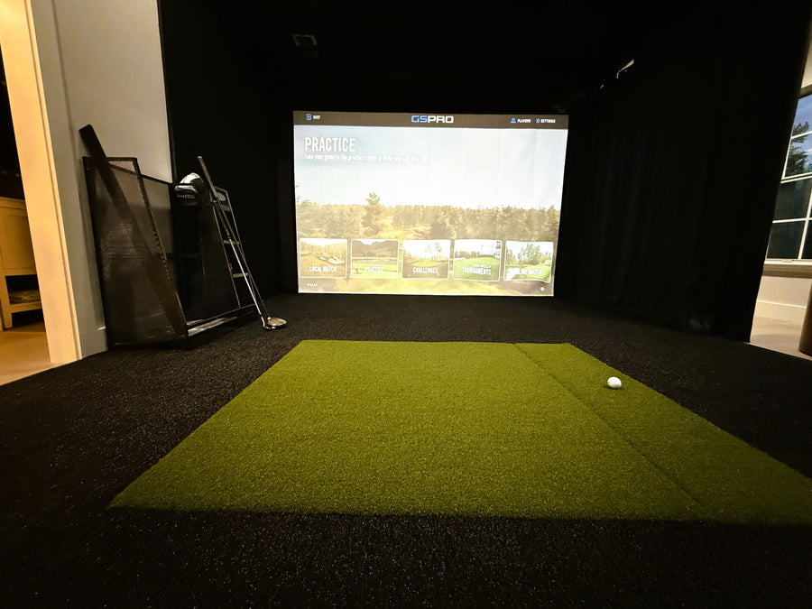 Indoor golf simulator with green turf and screen displaying a golf course.