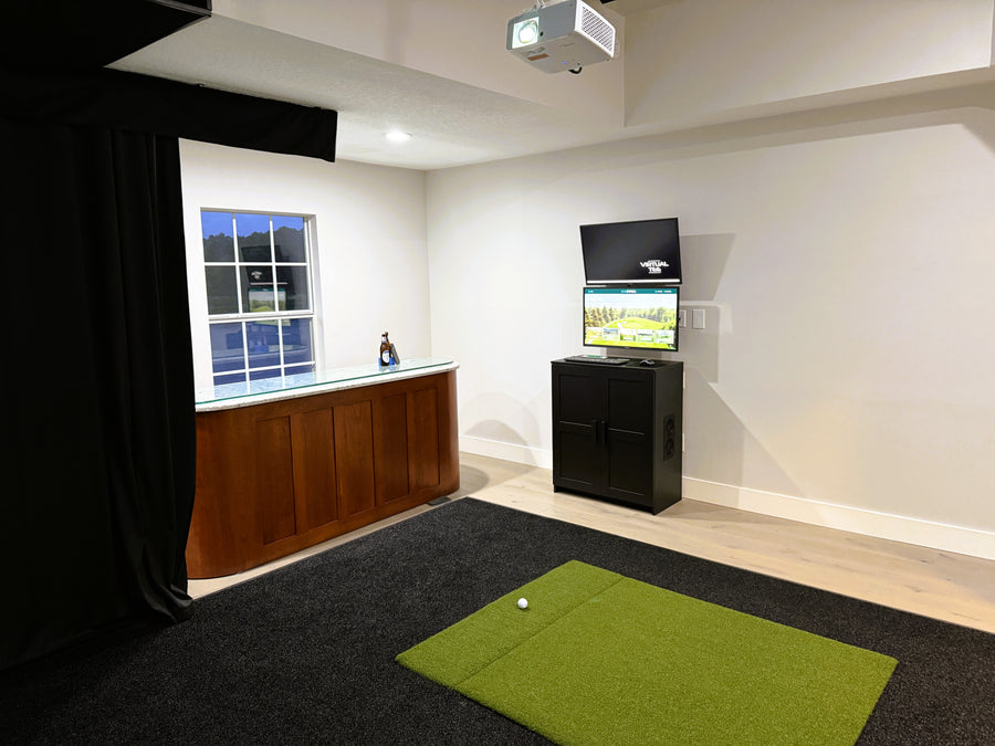 Golf simulator setup in a room with a green mat on the floor.