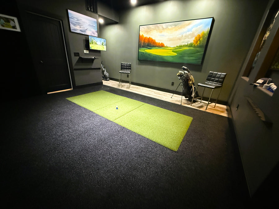 Indoor golf simulator setup with green mat and multiple screens displaying golf visuals.
