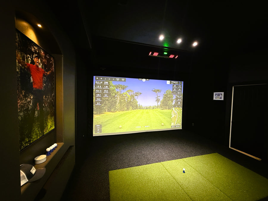 Indoor golf simulator setup with screen displaying a golf course and a green floor.