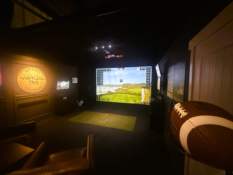 Indoor golf simulator room with virtual golf game on screen, surrounded by sports equipment.