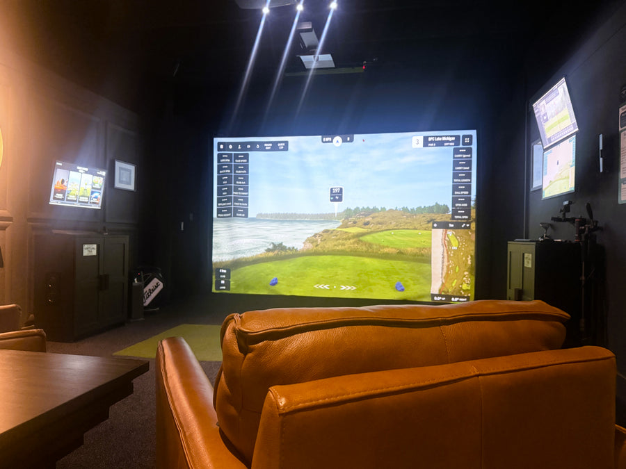 Indoor golf simulator setup with a large screen displaying a golf course.