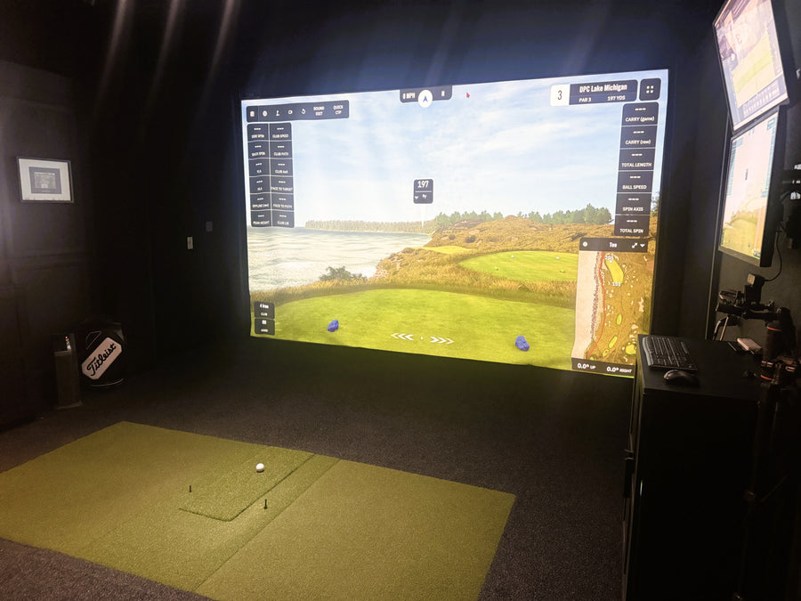 Golf simulator setup with screen displaying a golf course, remote control, and golf ball on a mat.