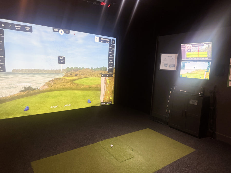 Golf simulator room with large screen displaying a golf course and small screen on wall.
