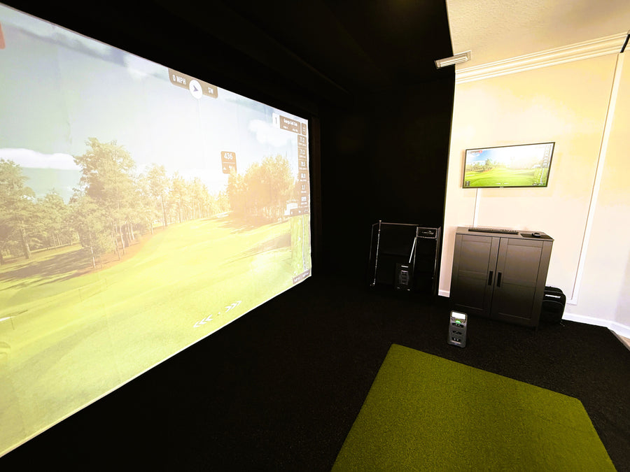 Indoor golf simulator setup with large screen and cabinet in a room.