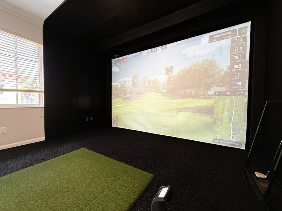 Indoor golf simulator setup with screen displaying a golf course.