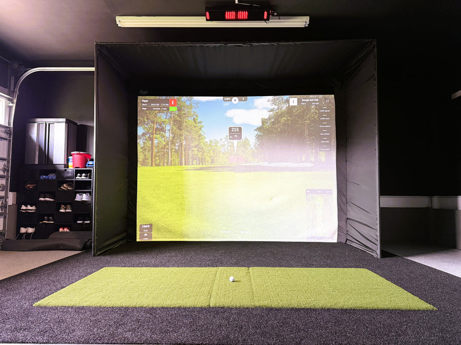 Golf simulator setup with screen displaying a golf course and a green mat on the floor.